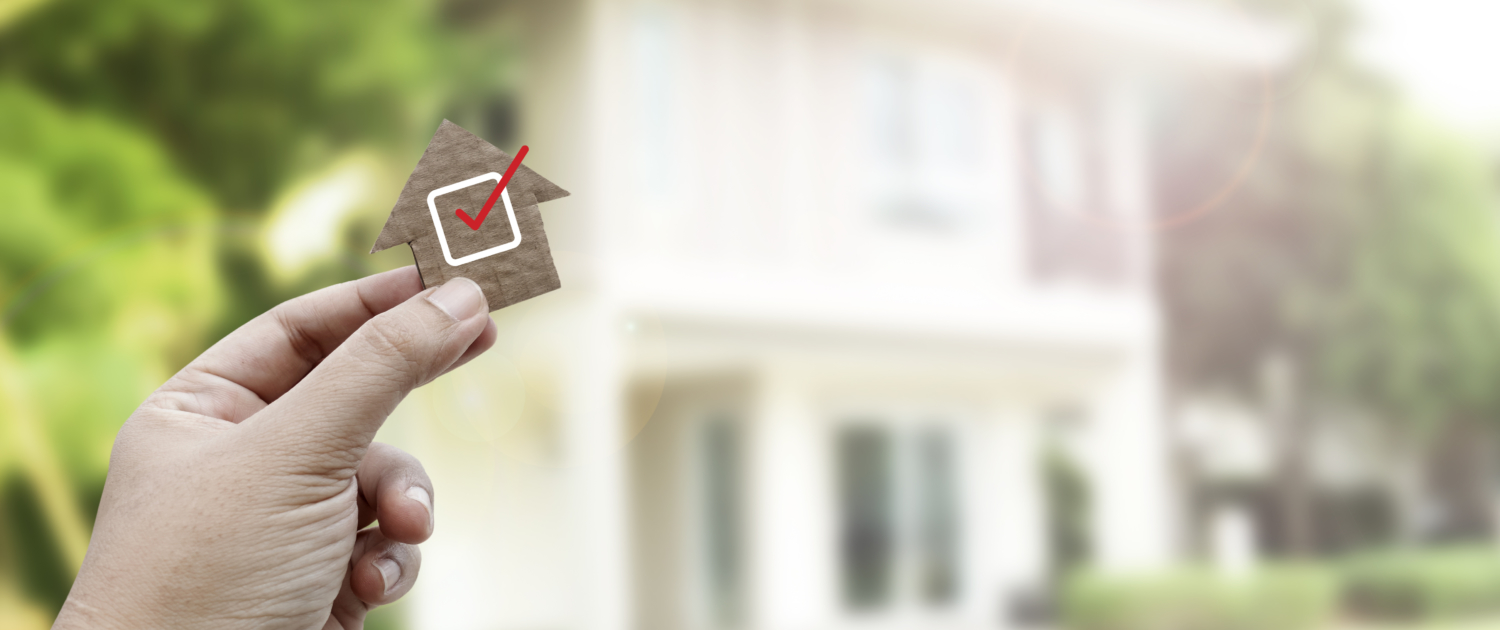 Hand holding brown paper , Home inspection Hand holding a wooden house cutout with a red checkmark in front of a home